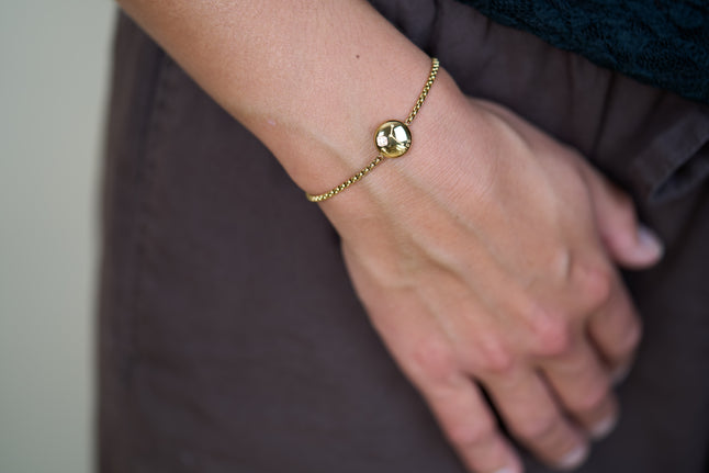 Gold zodiac charm bracelet on wrist with round pendant and small crystal detail