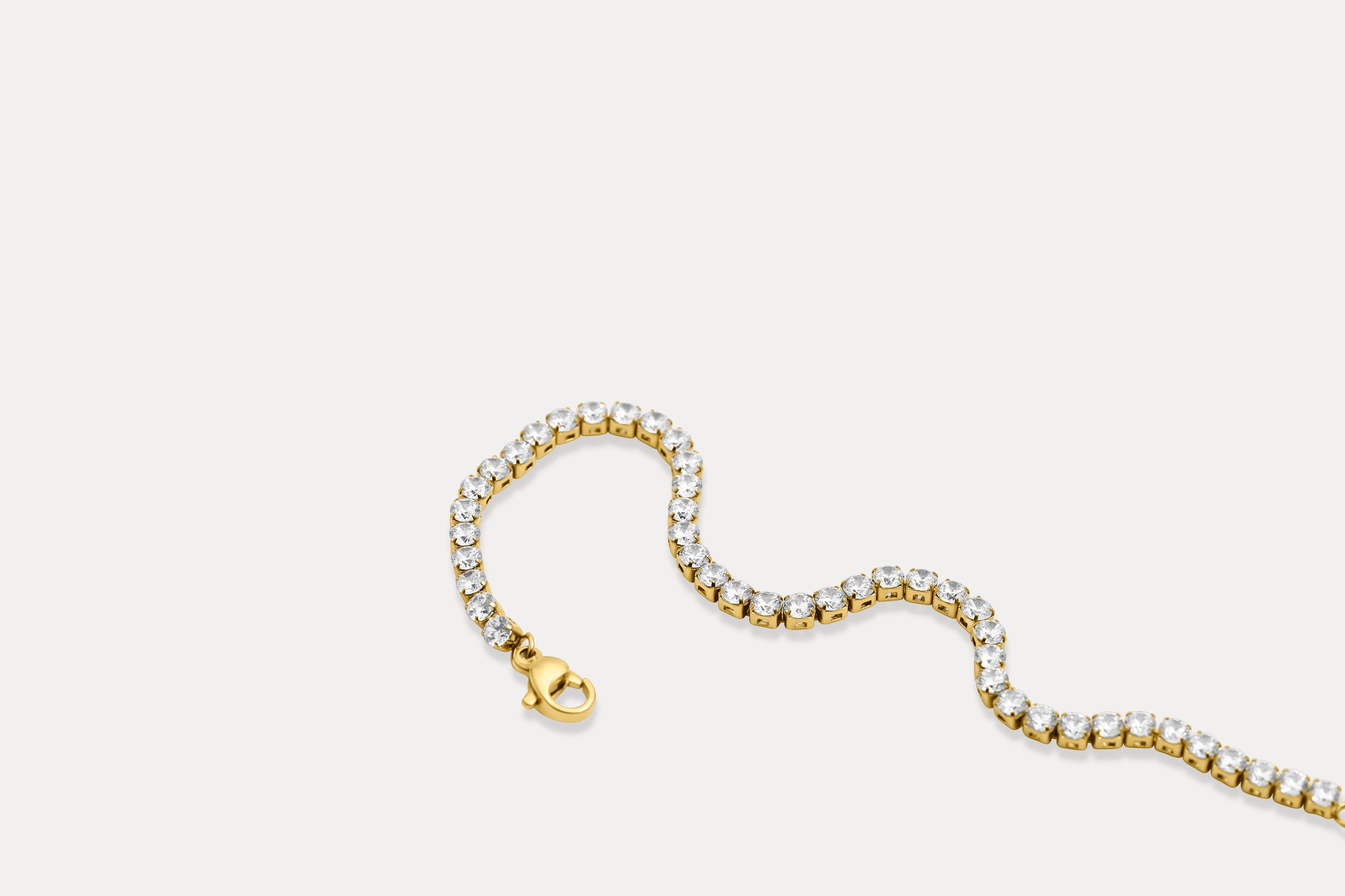 Gold tennis bracelet with clear rhinestone links and gold clasp, flat lay
