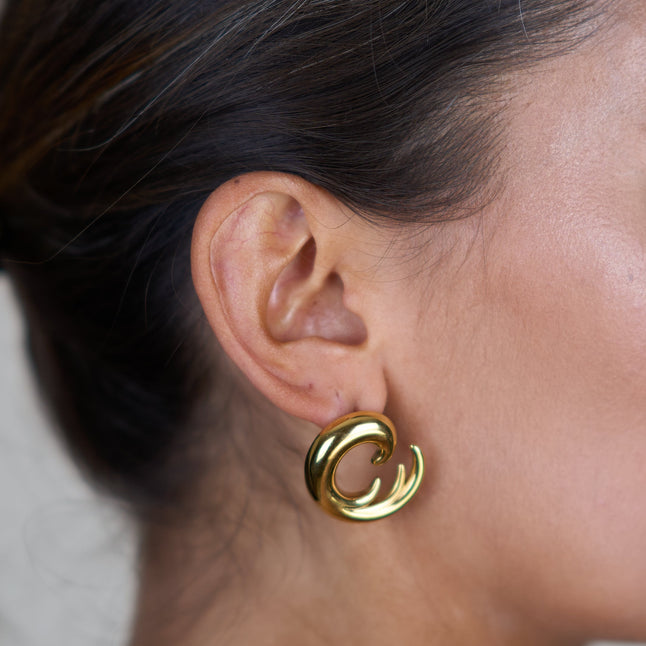Gold wave hoop earrings, close-up on ear