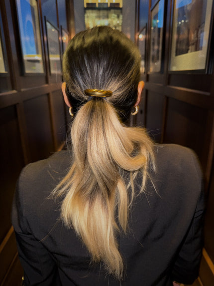 Gold hair tie securing a low ponytail, viewed from the back.
