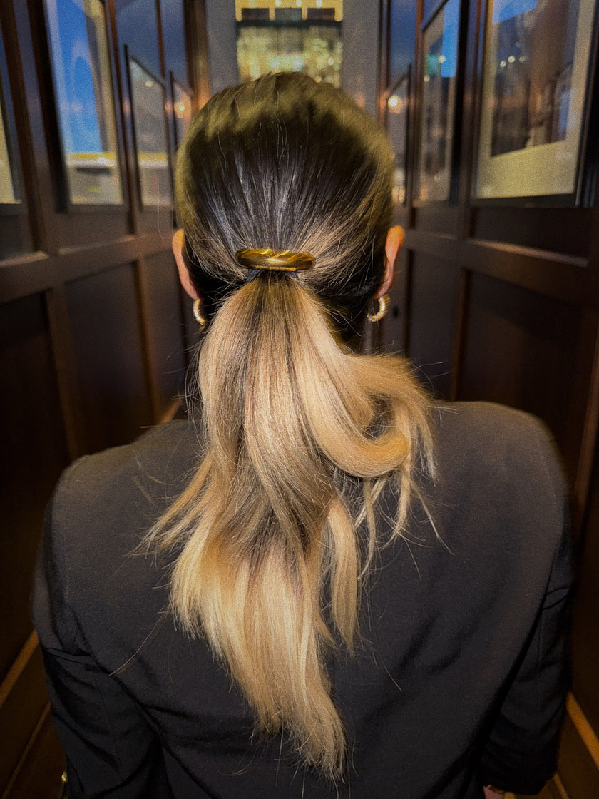 Gold hair tie securing a low ponytail, viewed from the back.
